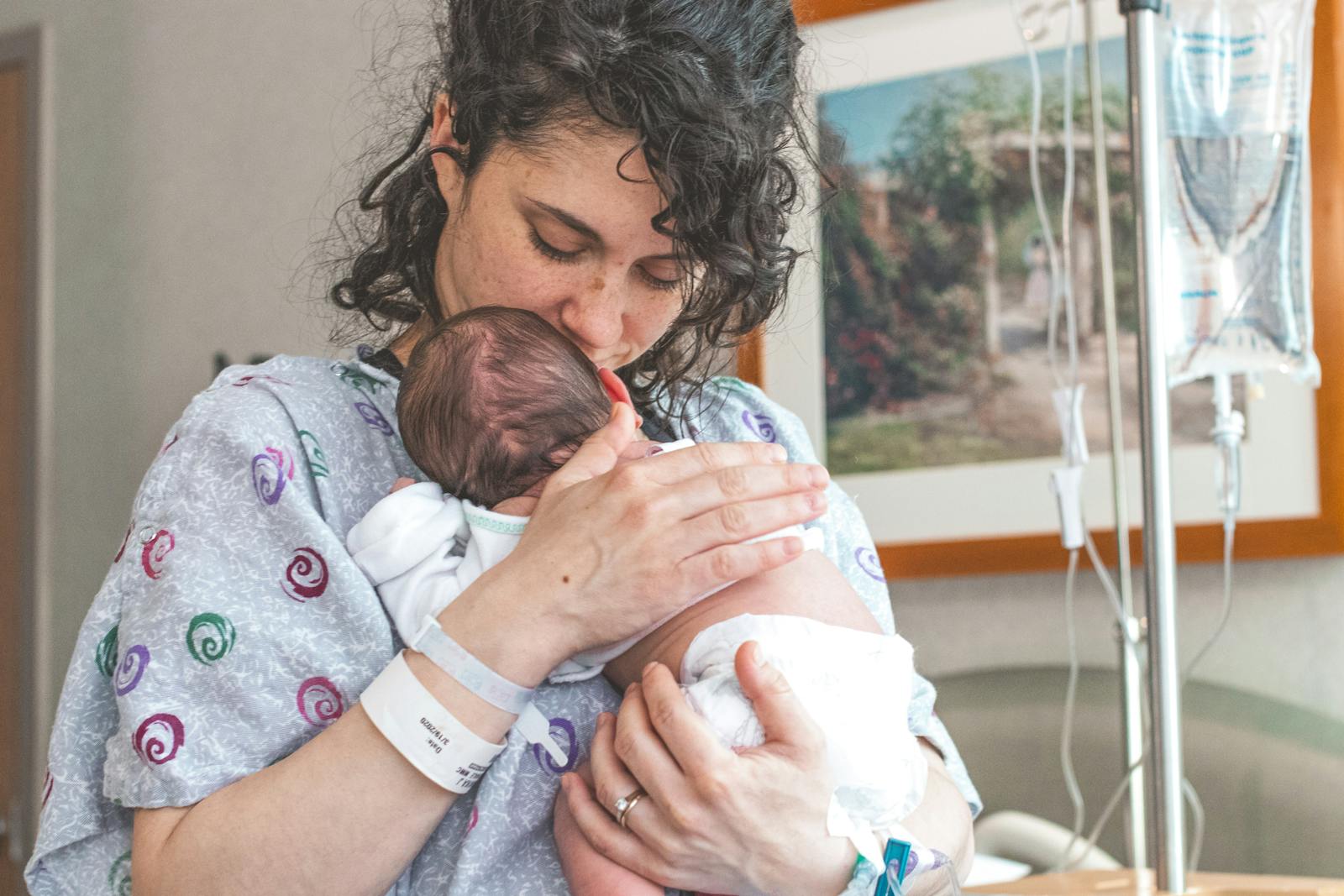 Mother gently holding newborn baby in hospital setting, showcasing warmth and love.